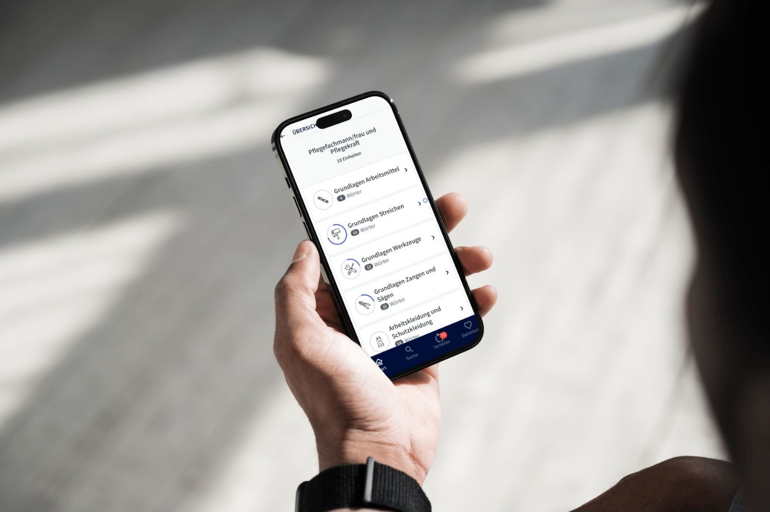 Eine Hand hält ein Smartphone, das die Lunes App und den Lernfortschritt anzeigt.
